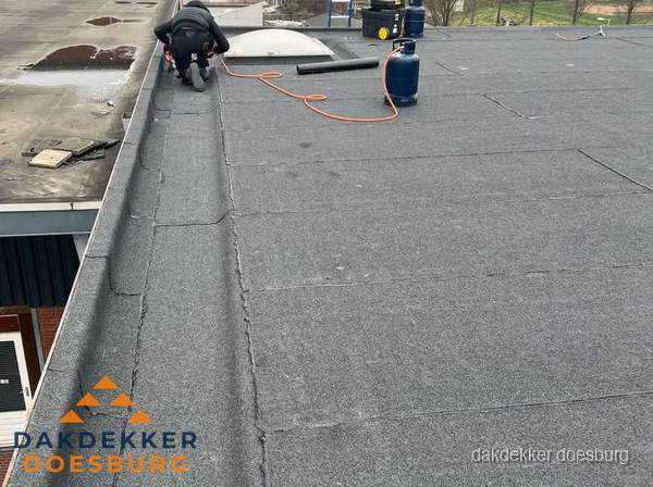 Dakdekker repareert bitumen dakbedekking op groot plat dak in Doesburg