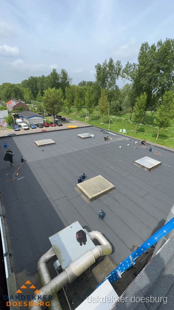 Dakdekker aan het werk op groot plat dak met bitumen in Doesburg